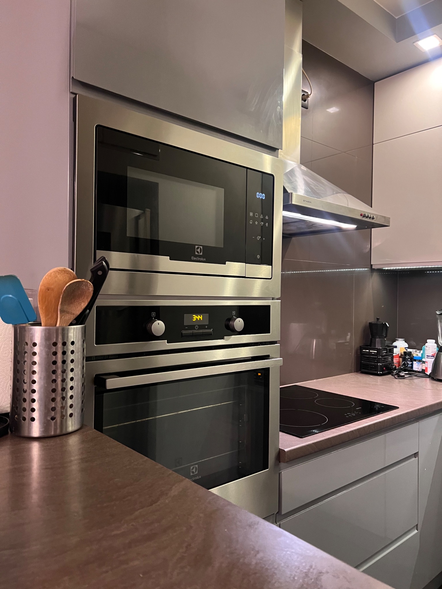 Wbudowany piekarnik i mikrofalówka Electrolux ze stali nierdzewnej w nowoczesnej kuchni z drewnianymi przyborami w metalowym pojemniku na blacie.