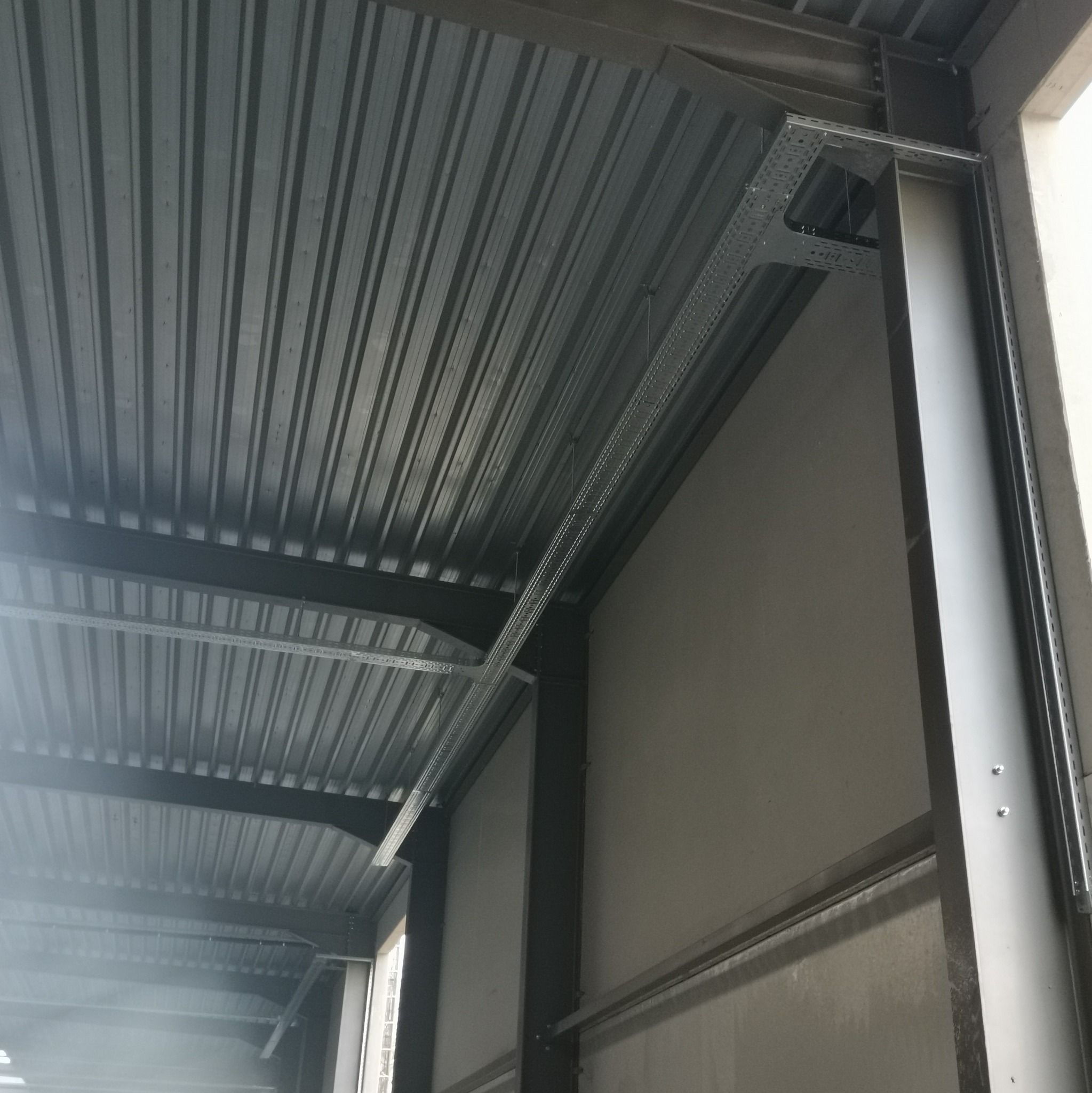 Metalowa konstrukcja sufitu z systemem koryt kablowych, widoczne elementy mocujące i łączenia, surowy stan wykończenia wnętrza.