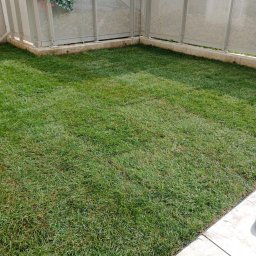 TRANSTECHNIK DZMITRY KARAVAI - Świeżo ułożona trawa z rolki na balkonie, otoczona metalową balustradą z elementami dekoracyjnymi z zielonych pnączy. Widok z góry, równomierne oświetlenie.