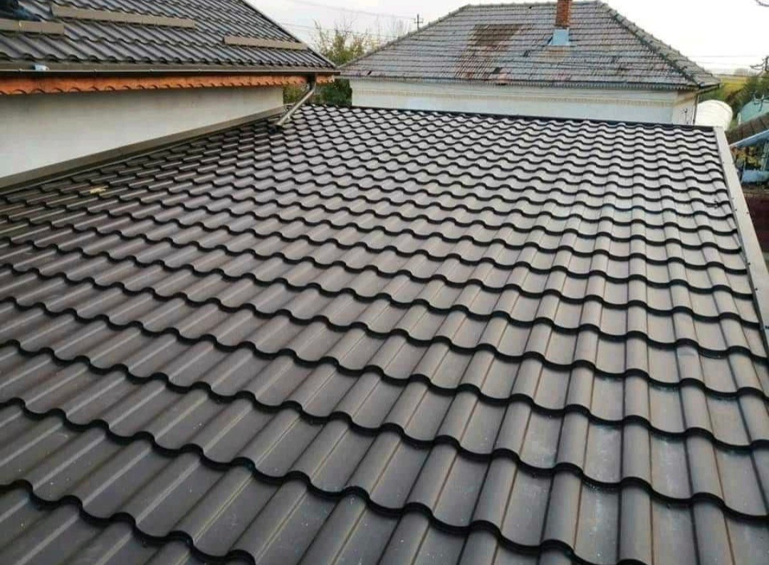 Dachówka metalowa w kolorze grafitowym, ułożona na dachu budynku mieszkalnego, widok z góry, w tle sąsiedni budynek z brązową dachówką.
