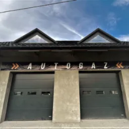Budynek warsztatu z dwoma bramami garażowymi i szyldem z napisem AUTO GAZ umieszczonym nad nimi, widok z dołu.