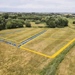 Działki budowlane z naniesionymi granicami i drogami dojazdowymi, widok z drona na otwartą przestrzeń z drzewami w tle.