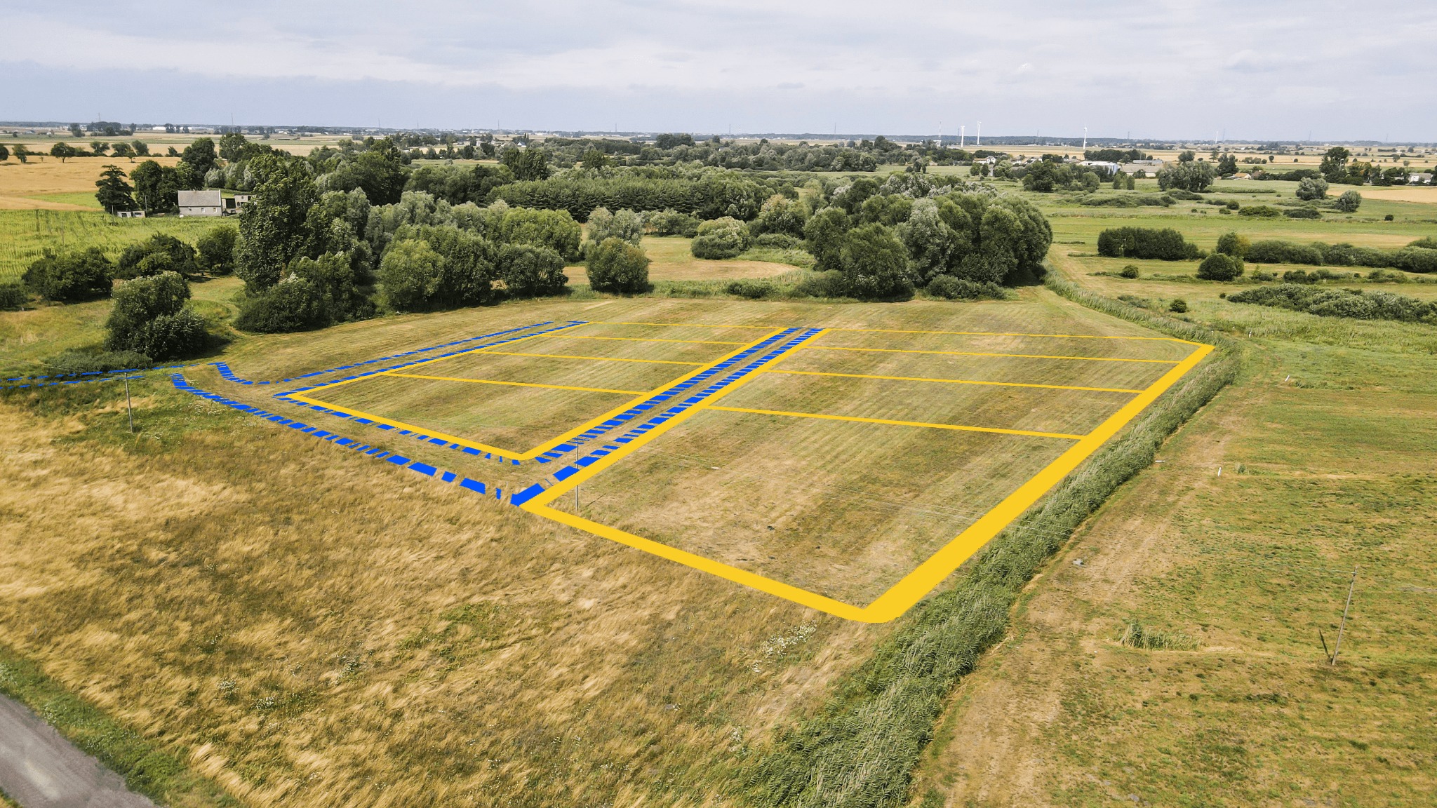 Działki budowlane z naniesionymi granicami i drogami dojazdowymi, widok z drona na otwartą przestrzeń z drzewami w tle.