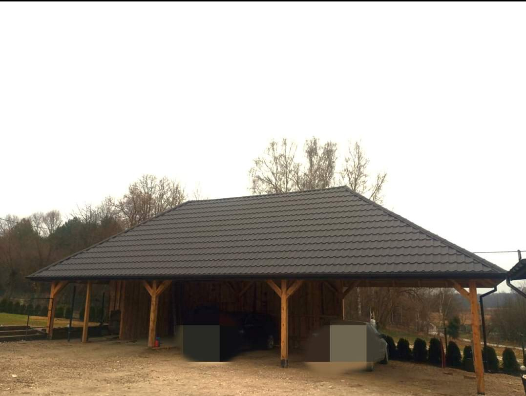Zadaszenie na dwa samochody z brązową blachą trapezową, drewniana konstrukcja z widocznymi belkami, w tle drzewa bez liści.