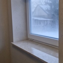 RakBud ogolno pracę remontowo budowlane. - Wnętrze z oknem i marmurowym parapetem. Ściany pokryte beżowym tynkiem strukturalnym. Za oknem widok na zasypany śniegiem dom.