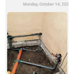 RakBud ogolno pracę remontowo budowlane. - Instalacja wodno-kanalizacyjna w trakcie montażu w narożniku pomieszczenia. Widoczne rury PCV, narzędzia i fragment ściany z uszkodzonym tynkiem. Prace remontowe w toku.