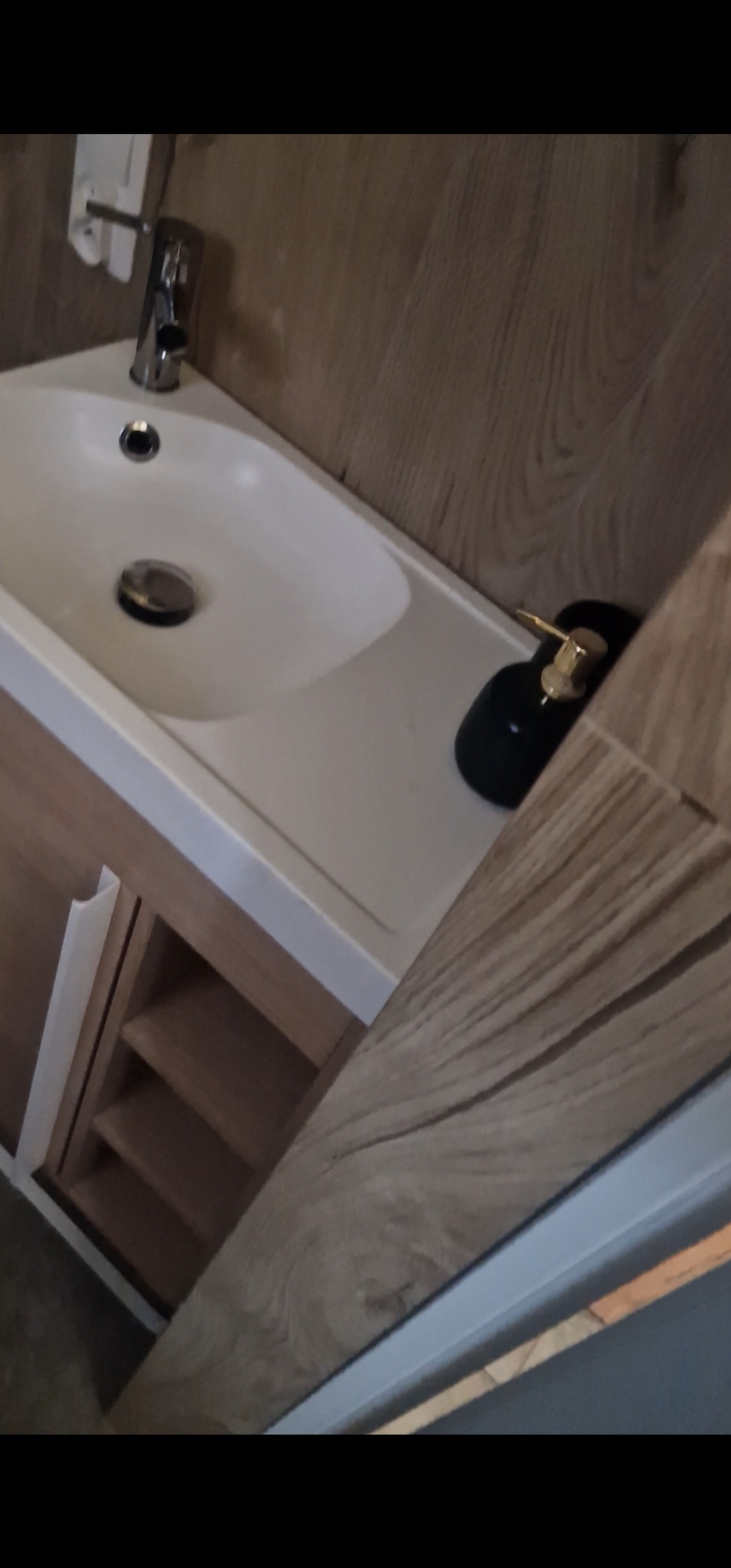 Nowoczesna umywalka nablatowa z szafką w odcieniach drewna, bateria chromowana i dozownik mydła w czerni ze złotymi akcentami. Wykończenie łazienki w stylu minimalistycznym.