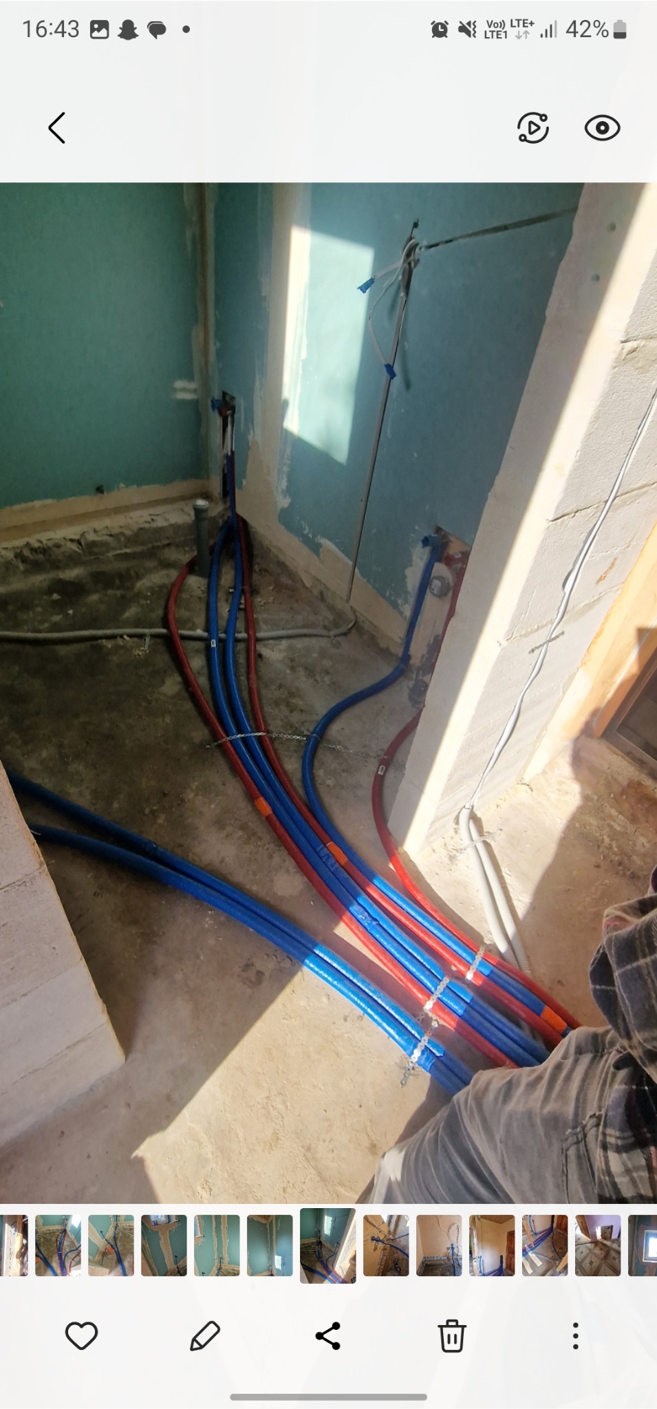 Instalacja wodna z rur PEX w kolorach niebieskim i czerwonym, ułożona na podłodze w trakcie remontu łazienki. Widoczne ślady po szpachlowaniu na ścianach.