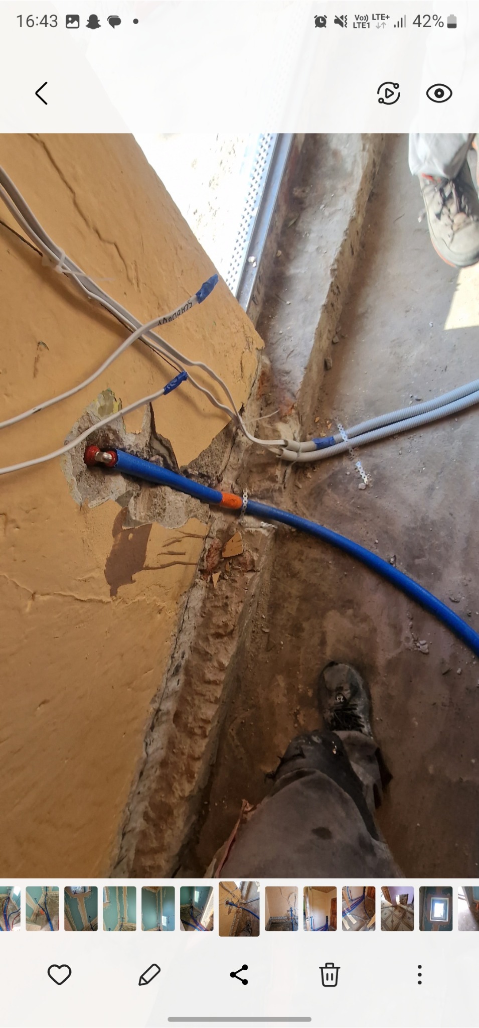 Instalacja wodna i elektryczna w trakcie remontu. Niebieska rura wodna przymocowana do ściany, białe kable elektryczne. Widoczne ślady po kuciu w ścianie i podłodze.