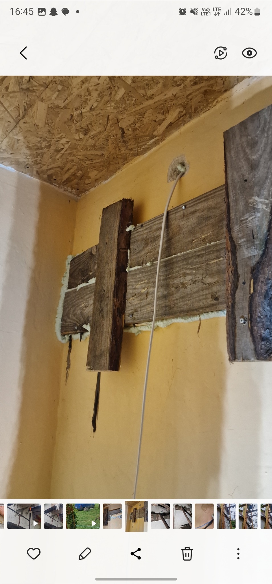 Montaż drewnianej konstrukcji na ścianie z widoczną pianką montażową i wystającym przewodem elektrycznym. Fragment sufitu z płyty OSB.