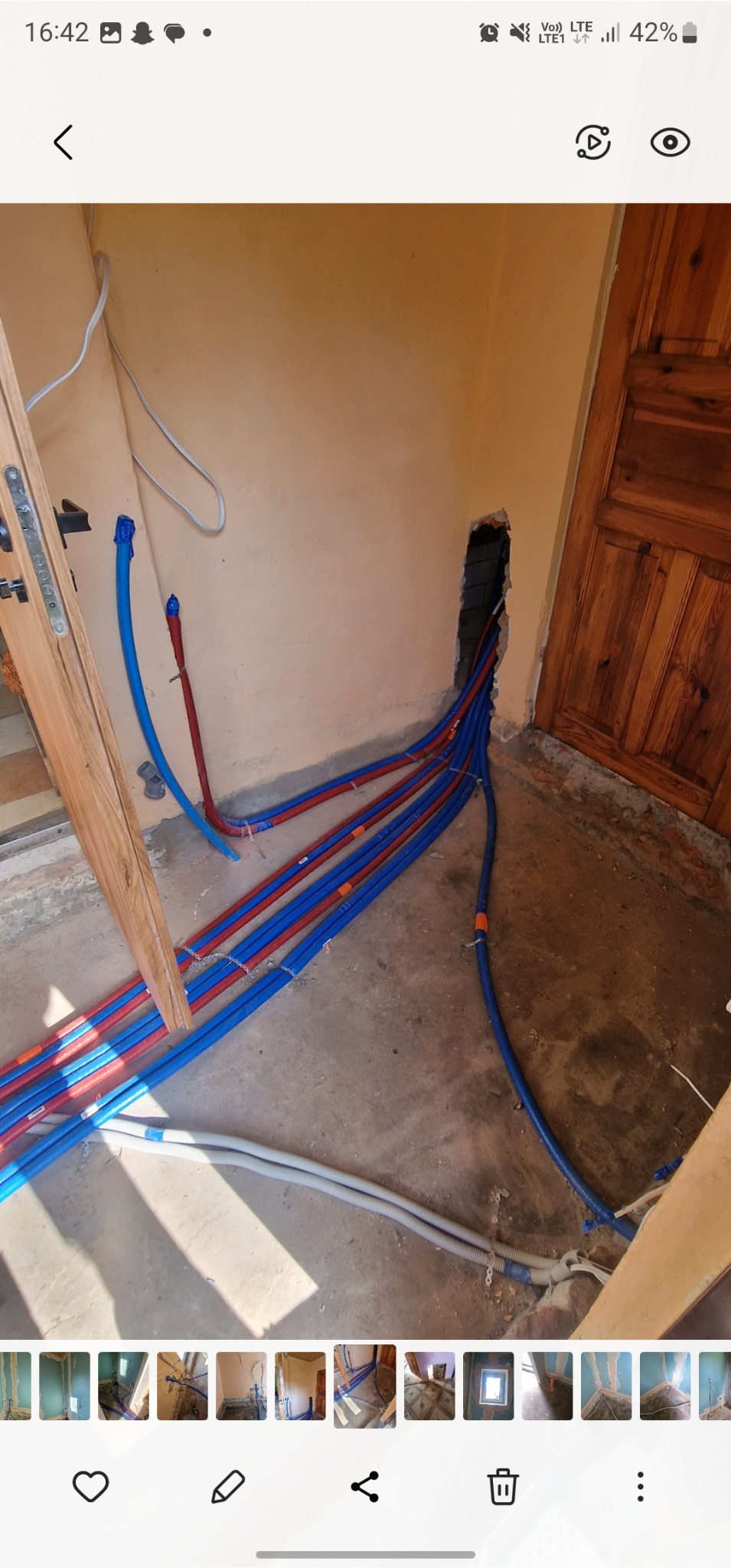 Instalacja wodna: rury PEX w kolorach niebieskim i czerwonym prowadzone wzdłuż ściany, w otworze w ścianie. Widoczne elementy montażowe i fragment podłogi.