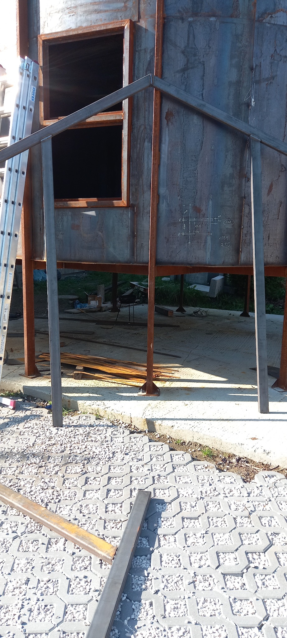 Konstrukcja stalowa hali w trakcie budowy w Pakułach, widoczna drabina oparta o ścianę oraz rysunki techniczne naniesione na poszycie hali.