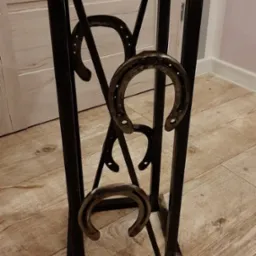 Metalowy kwietnik z drewnianym blatem i dekoracyjnymi podkowami, spawany z profili, widoczne spawy.