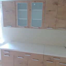 Nowoczesna zabudowa kuchenna z drewnopodobnymi frontami i przeszklonymi szafkami górnymi, minimalistyczne srebrne uchwyty, jasny blat.