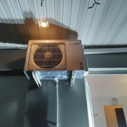 Zamontowana jednostka wewnętrzna klimatyzacji Mitsubishi Electric na szarej ścianie, widoczna instalacja odprowadzająca skropliny, sufit z panelami PCV.