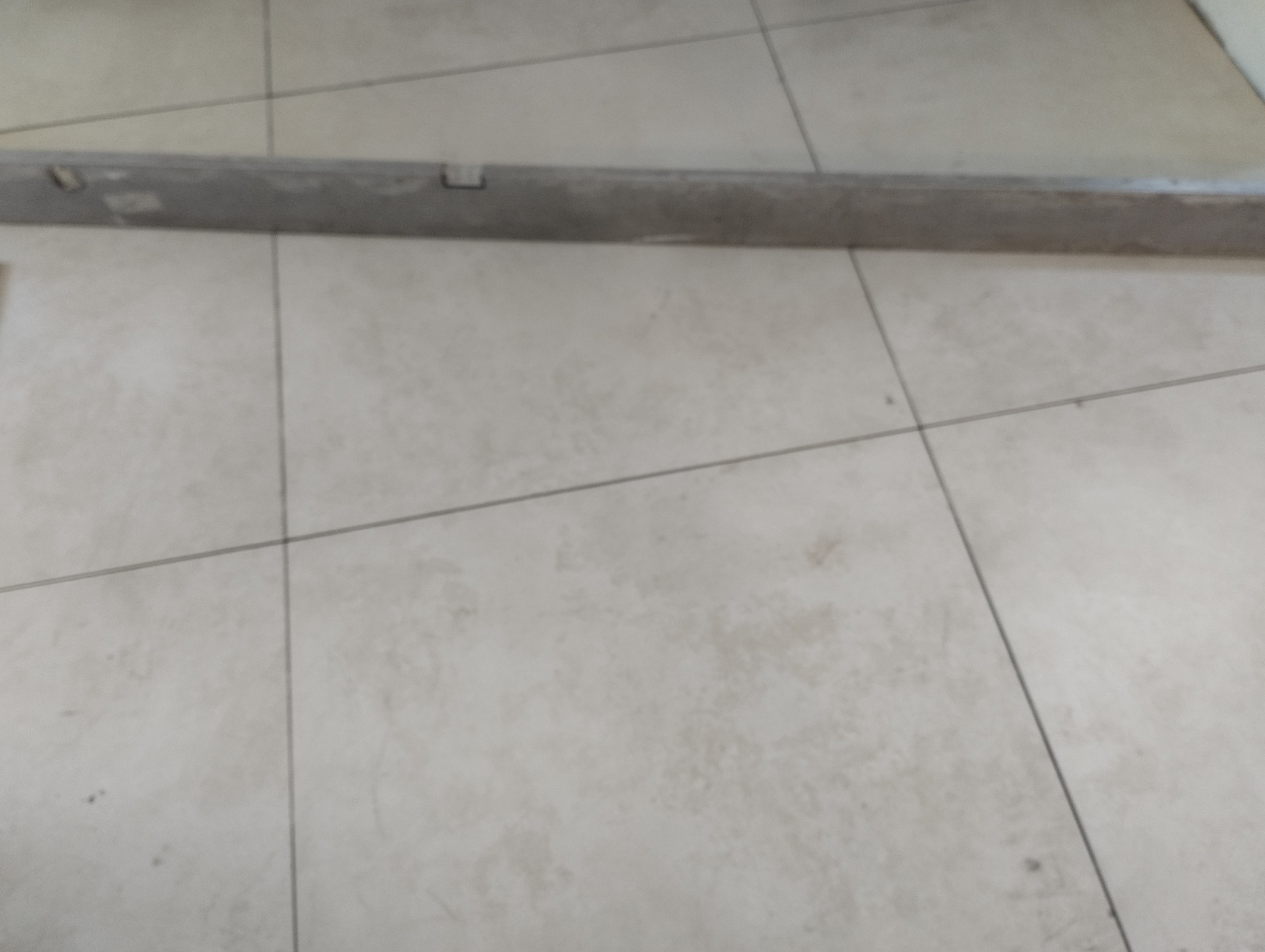 Ułożone jasne płytki podłogowe z widoczną poziomicą murarską, sprawdzającą równość powierzchni.