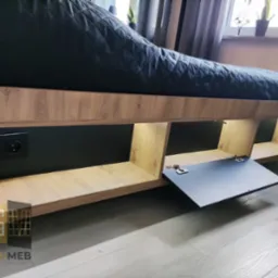 Nisko zawieszona antresola z oświetleniem LED, drewnianym wykończeniem i czarnymi elementami, w tym otwartą szafką z widocznymi zawiasami i gniazdkiem elektrycznym z włącznikiem.