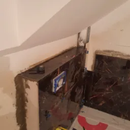 Montaż płytek imitujących marmur w łazience ze stelażem podtynkowym; widoczne kliny i poziomica