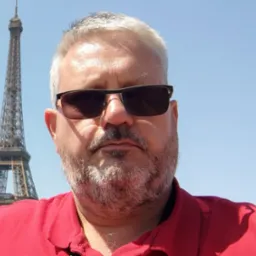 Mężczyzna w okularach przeciwsłonecznych robiący selfie z Wieżą Eiffla w tle, słoneczny dzień.