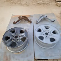 Felga i wahacz samochodowy przed i po piaskowaniu/malowaniu. Po lewej: stan skorodowany. Po prawej: element po renowacji, pokryty szarym podkładem.