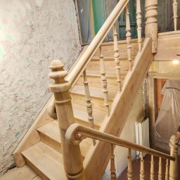 Fresz Natalia Loc - Drewniane schody z balustradą w surowym stanie, widoczne ślady prac remontowych na ścianach. Elementy schodów o frezowanych detalach.
