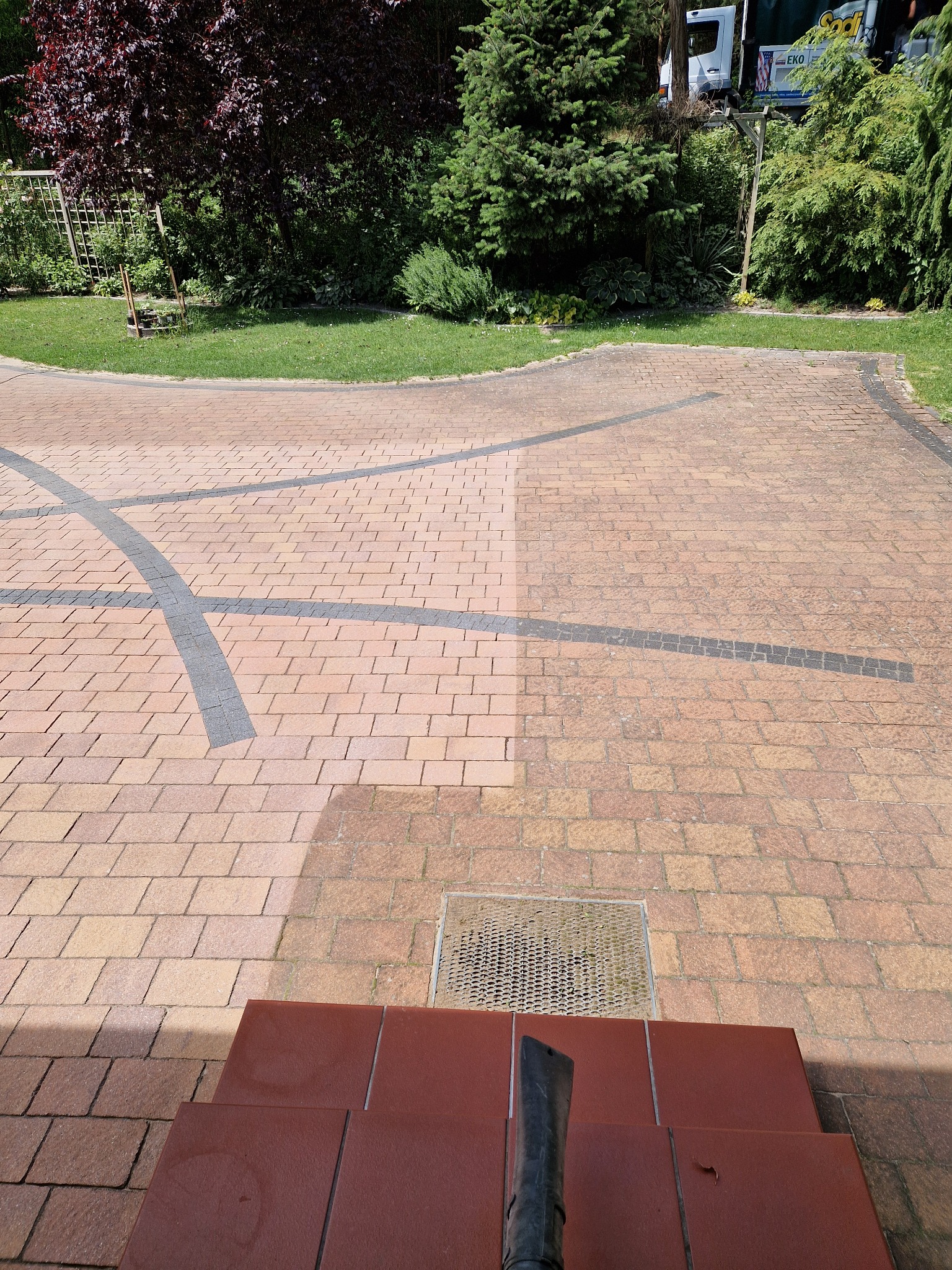 Częściowo umyta kostka brukowa w Zwierzynie, z widocznym kontrastem między czystą a brudną powierzchnią, zarys schodów i fragment buta roboczego w dolnej części kadru.