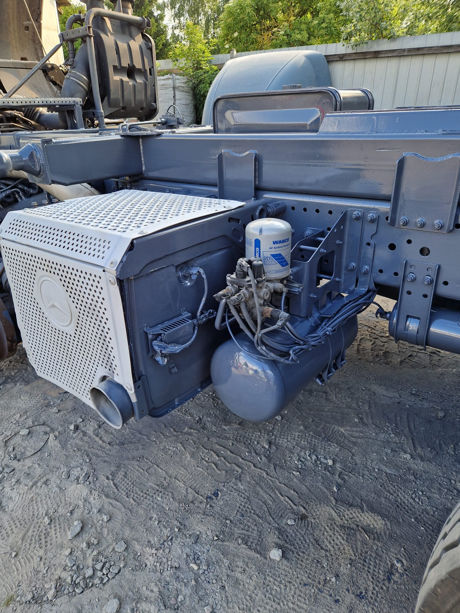 Szare podwozie ciężarówki z elementami układu pneumatycznego i chłodnicą z logo Mercedes, po konserwacji, na szutrowym podłożu.