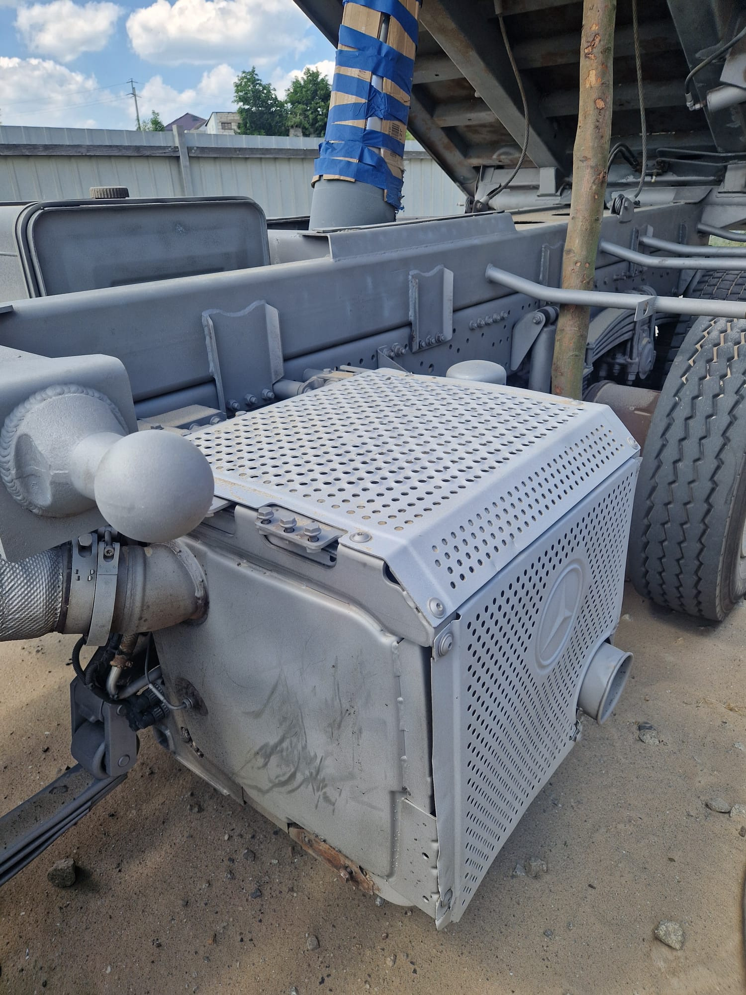 Szare elementy podwozia ciężarówki po piaskowaniu i malowaniu, widoczne detale konstrukcji i opona. Oznakowanie Mercedes na boku.