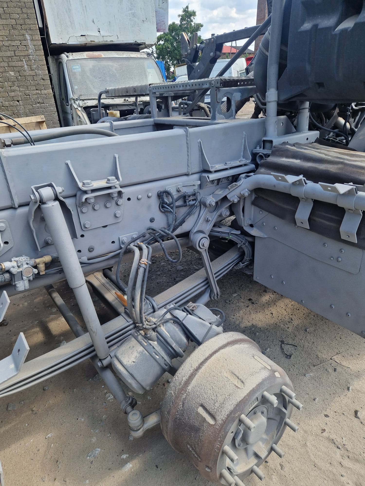 Szare podwozie ciężarówki w trakcie renowacji, widoczne elementy zawieszenia, osie i rama. Detale pokryte pyłem, co sugeruje etap piaskowania lub przygotowania do malowania.