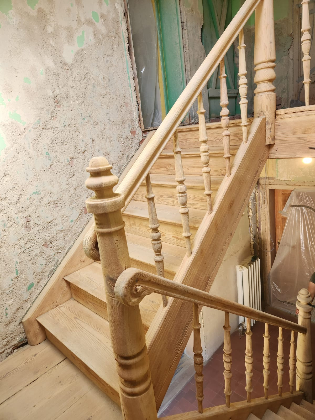 Drewniane schody z balustradą w surowym stanie, widoczne ślady prac remontowych na ścianach. Elementy schodów o frezowanych detalach.