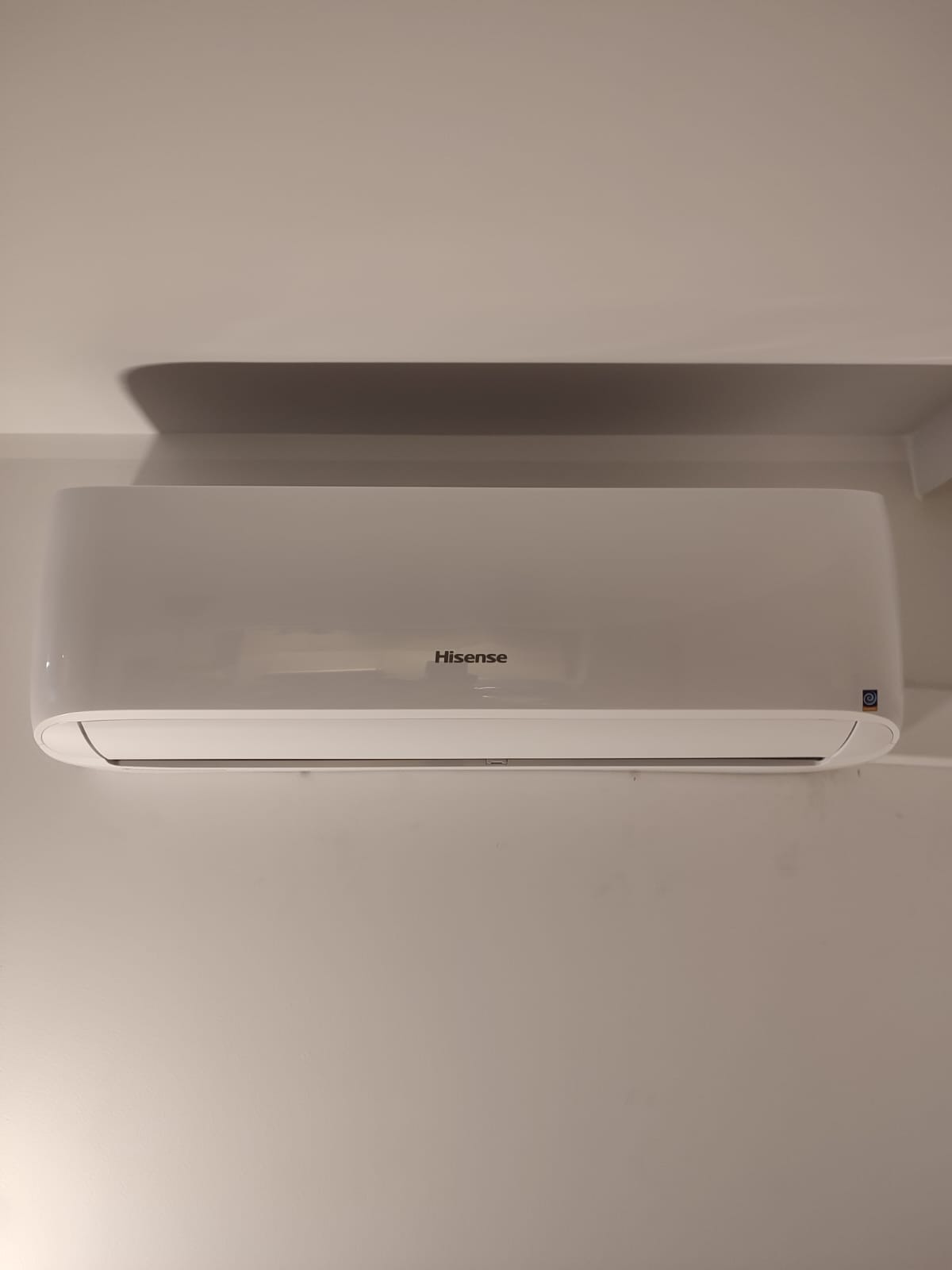 Biała jednostka wewnętrzna klimatyzacji marki Hisense zamontowana na jasnej ścianie, widoczny cień na suficie.