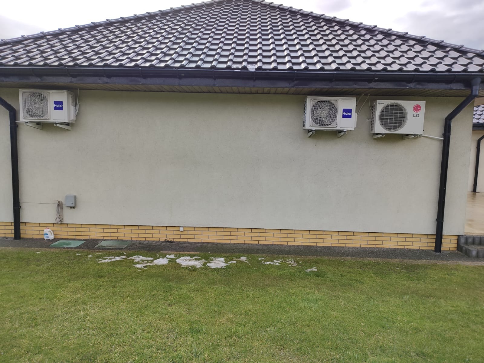 Trzy jednostki zewnętrzne klimatyzacji (Haier i LG) zamontowane na elewacji budynku we Włocławku, widoczne z poziomu trawnika.