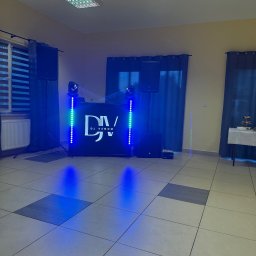 VENOM WORKS WŁADYSŁAW CHWASTEK - Ustawiony sprzęt DJ'ski z podświetleniem LED w sali z oknami i zasłonami. Widoczne głośniki, mikser, oświetlenie i logo 'DJ Venom'.  Podłoga wyłożona płytkami.