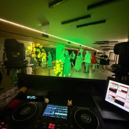VENOM WORKS WŁADYSŁAW CHWASTEK - DJ na weselu: parkiet pełen tańczących gości oświetlony zielonymi światłami, widok zza konsoli DJ-skiej Numark Mixstream Pro z laptopem.