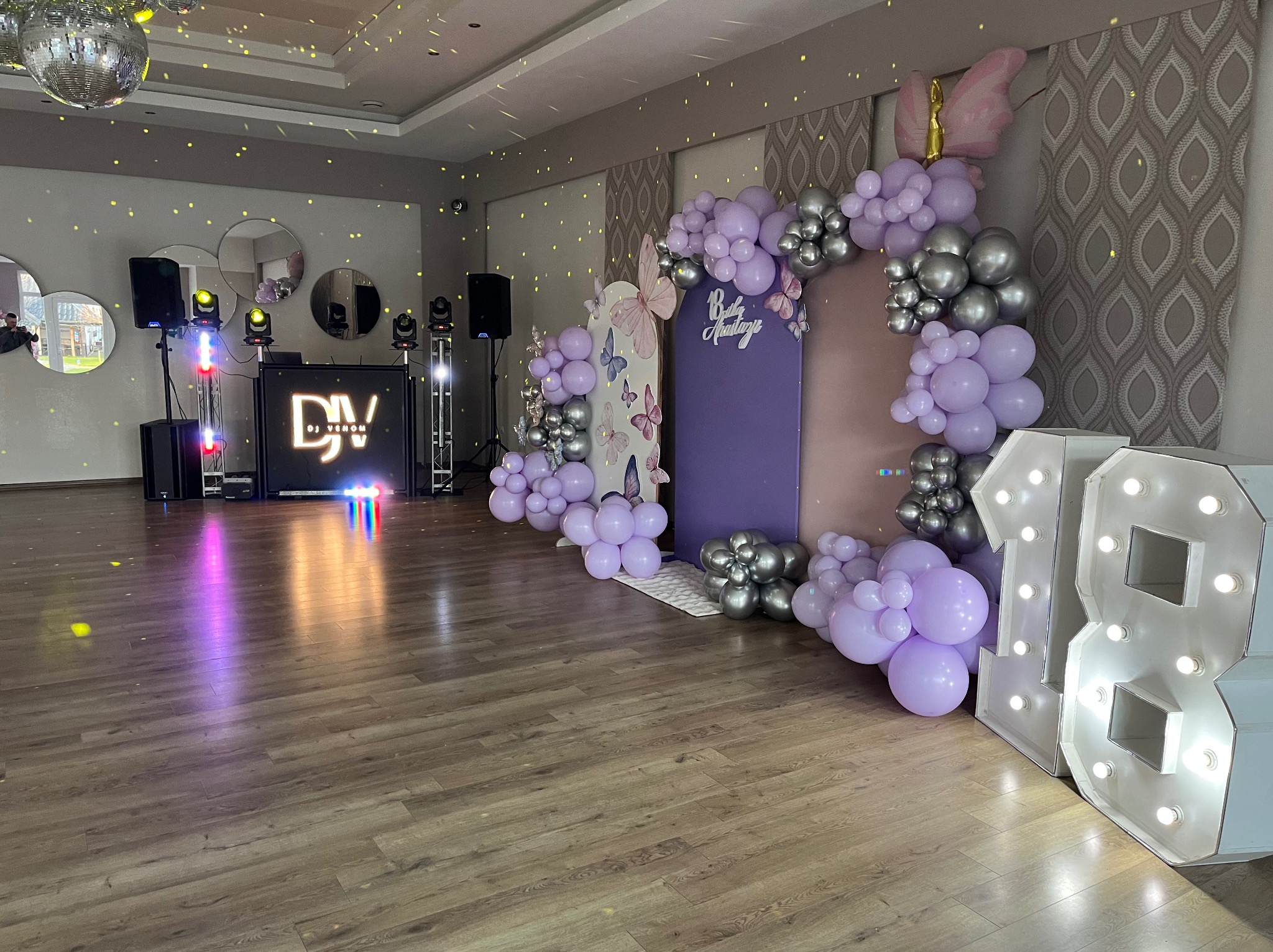 Dekoracja sali na osiemnaste urodziny z balonami w odcieniach fioletu i srebra, podświetlane cyfry '18', parkiet, w tle sprzęt DJ-ski z oświetleniem.