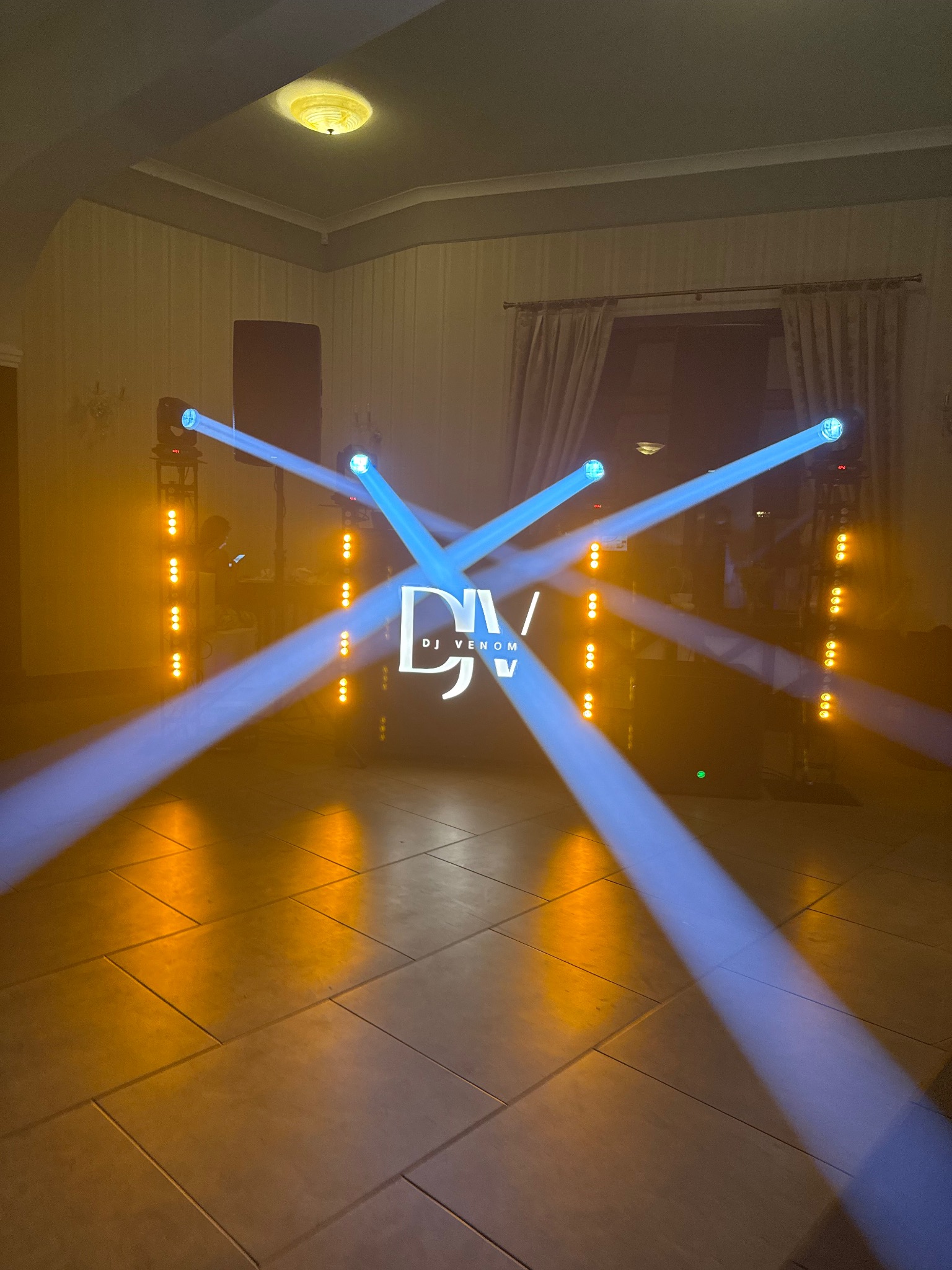 Scena z nagłośnieniem DJ Venom, oświetlona niebieskimi i pomarańczowymi reflektorami, tworzącymi efektowny pokaz świetlny na parkiecie.