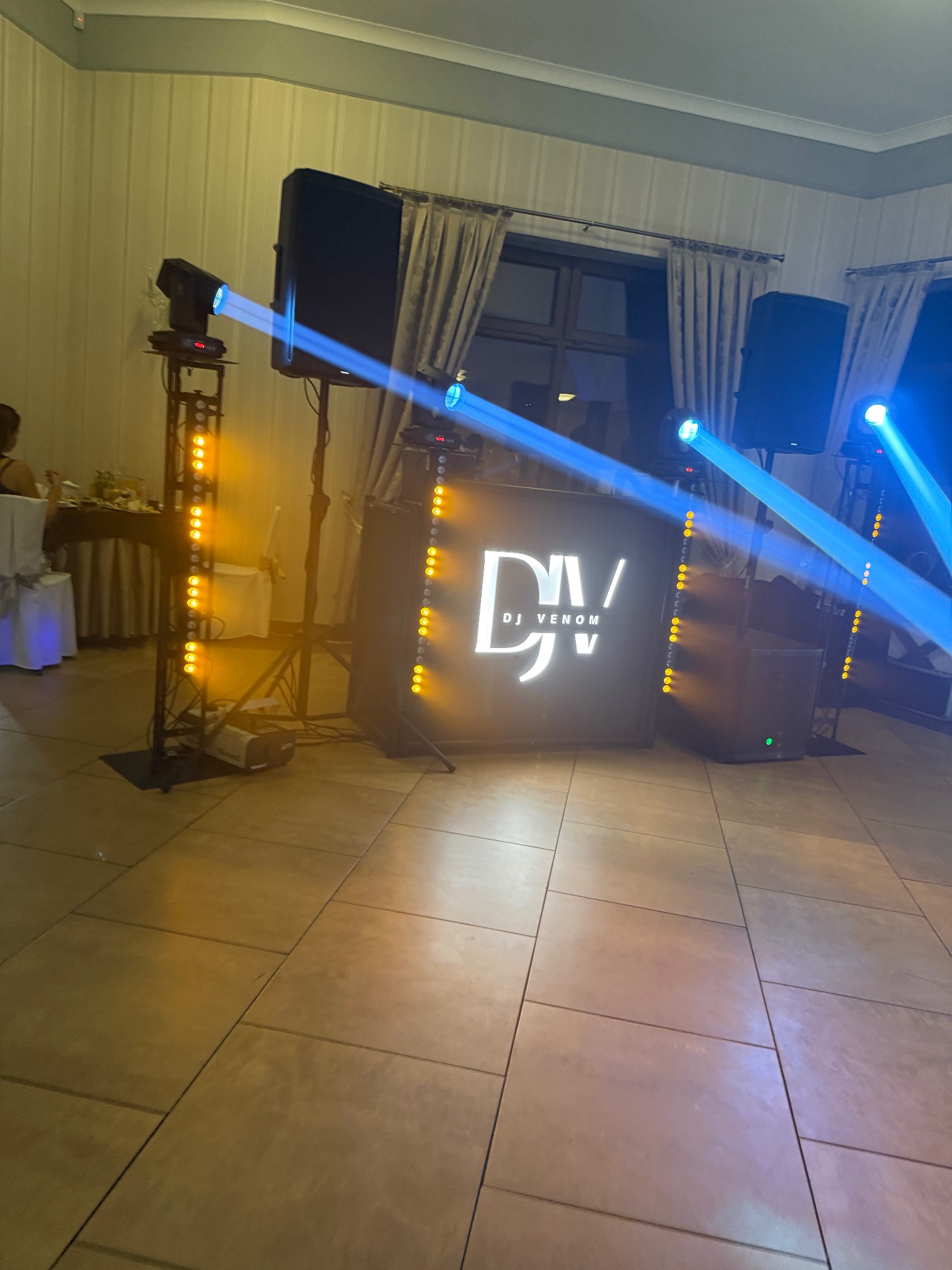 Oświetlenie sceniczne z logo DJ Venom, kolumny głośnikowe i reflektory na parkiecie. Dynamiczne niebieskie i żółte światła tworzą klubową atmosferę.