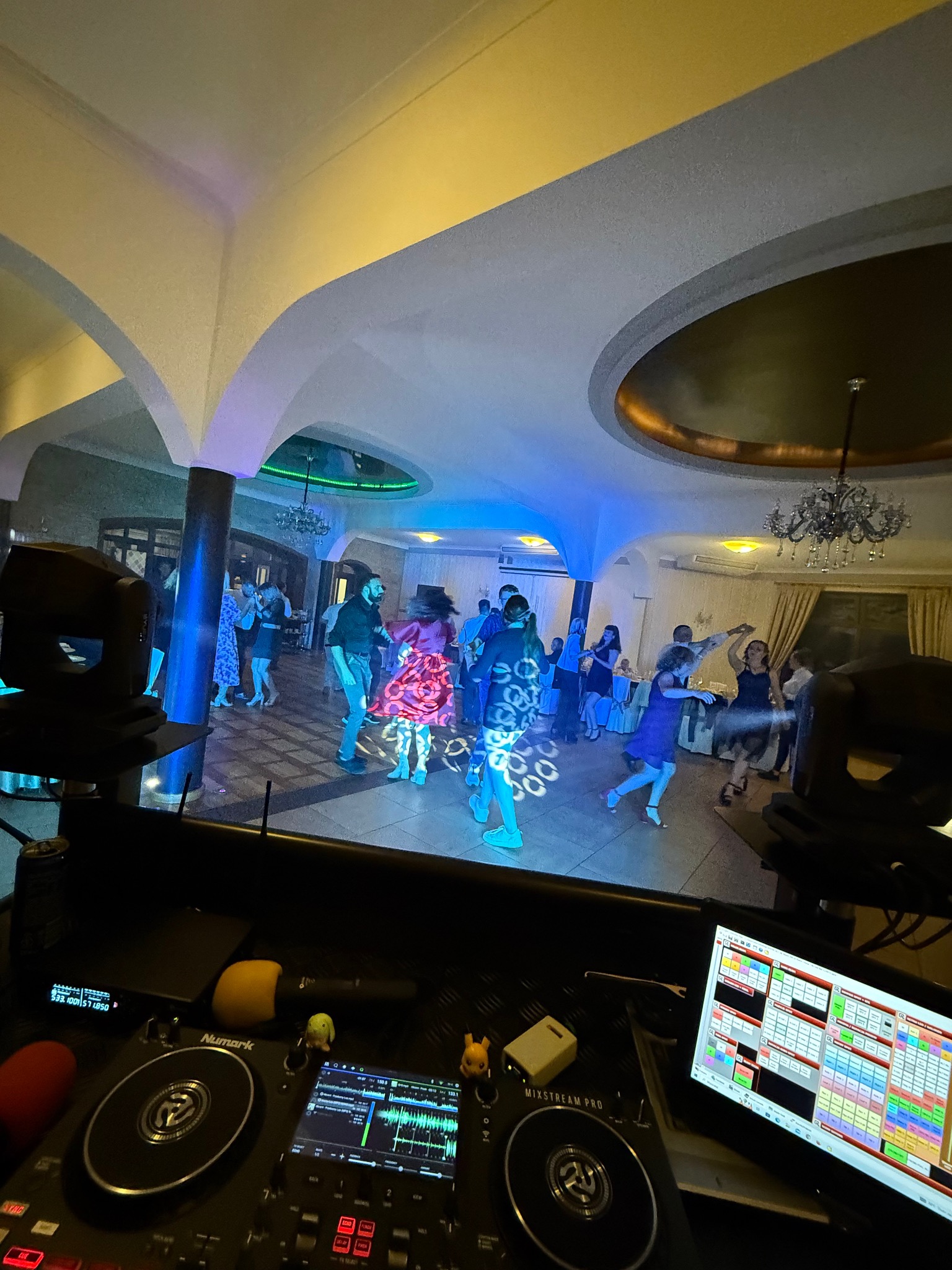 Parkiet taneczny z DJ-ką w tle, ludzie bawią się w oświetlonym lokalu. Widoczne elementy sprzętu DJ-skiego: mikser, laptop.