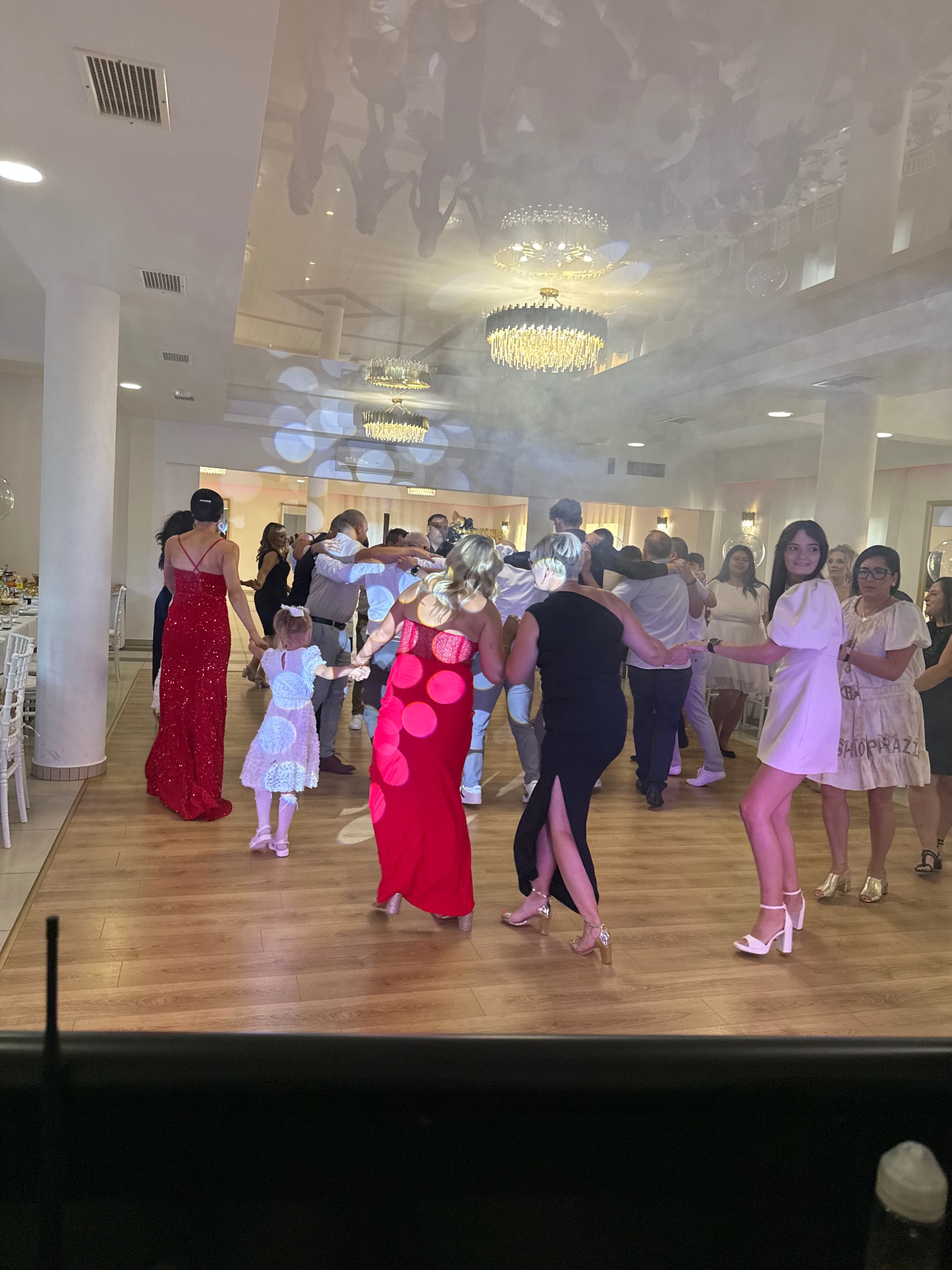 Parkiet i tańczący goście w sali balowej z kolumnami, oświetleniem punktowym i lustrzanym sufitem, tworzącym odbicia. W tle widoczne stoły z zastawą.