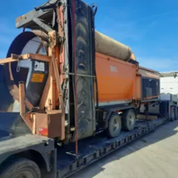 Pomarańczowy zestaw do przesiewania i transportu materiałów sypkich na niskopodwoziowej naczepie, widoczny znak ostrzegawczy w języku niemieckim.