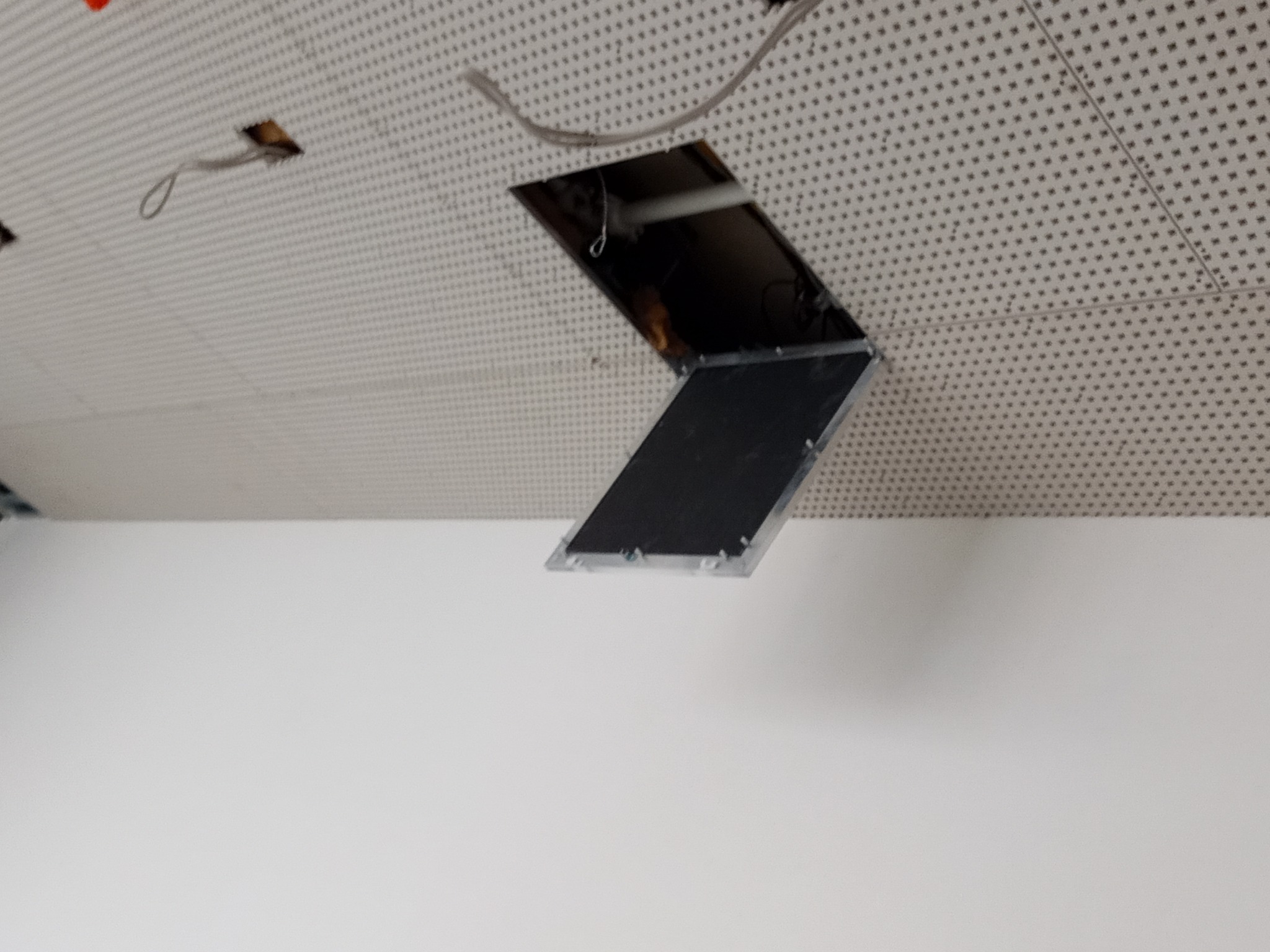 Otwarty fragment sufitu podwieszanego kasetonowego, ukazujący instalacje powyżej, z widocznymi kablami i przewodami.