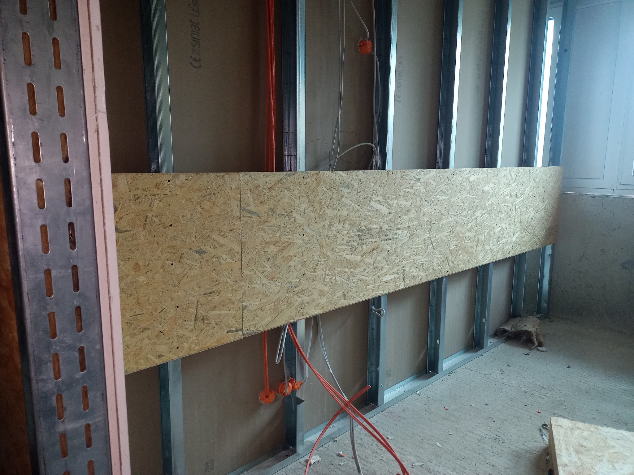 Montaż konstrukcji ściany działowej z profili stalowych i płyty OSB, widoczne przewody elektryczne i puszki instalacyjne.