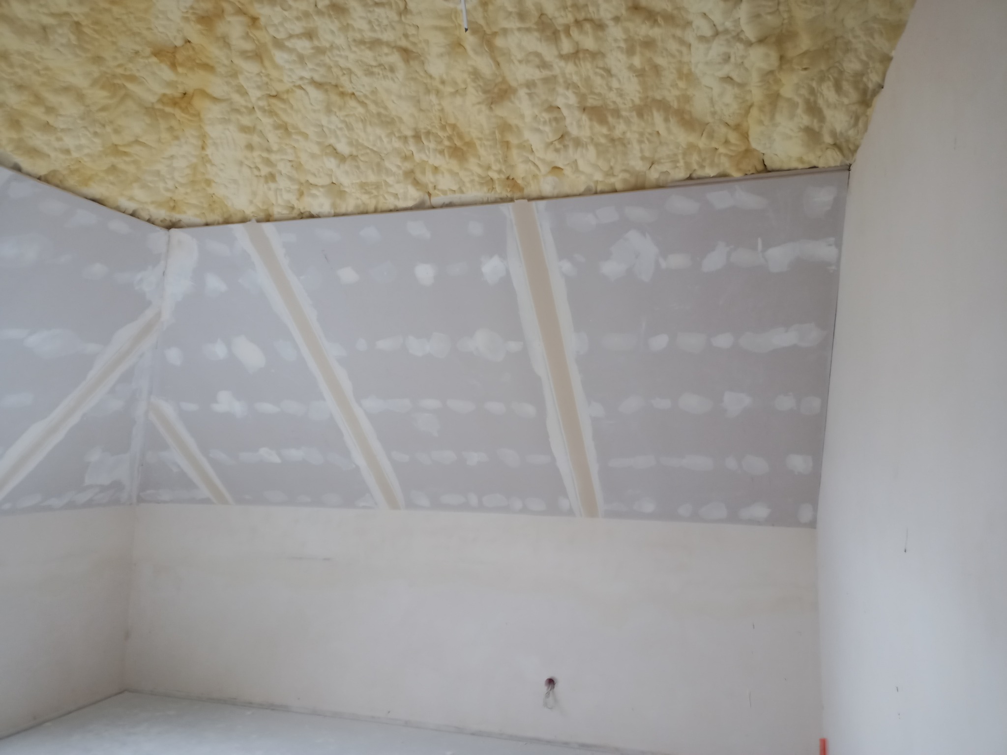 Poddasze w trakcie wykańczania: izolacja pianką na skosach dachu, ściany wyłożone płytami z widocznymi łączeniami przed szpachlowaniem.