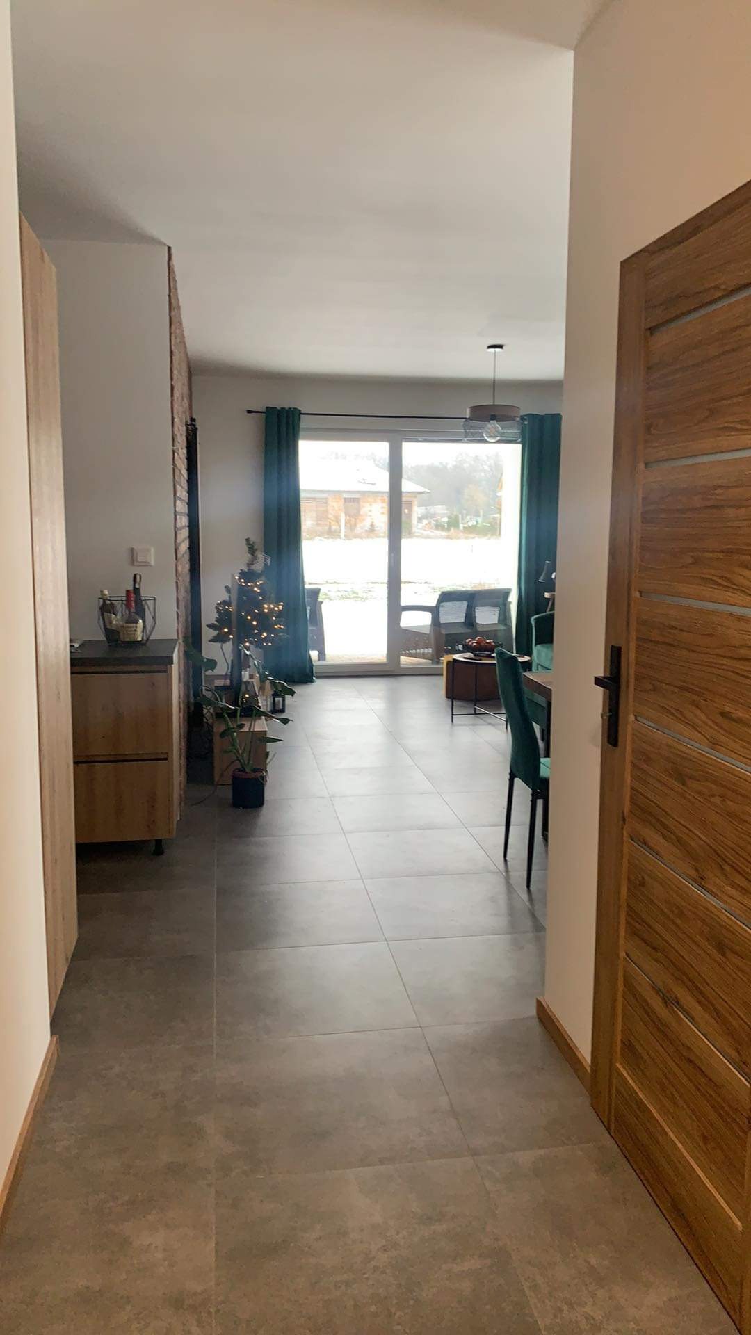 Ułożone szare płytki podłogowe w korytarzu domu w Poznaniu, widok na salon z dekoracjami świątecznymi i oknem na ogród.