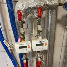 Dwa liczniki ciepła SanTech Q heat 5.5 zamontowane na rurach grzewczych z izolacją aluminiową, z czerwonymi zaworami Diamond Sp. z o.o.