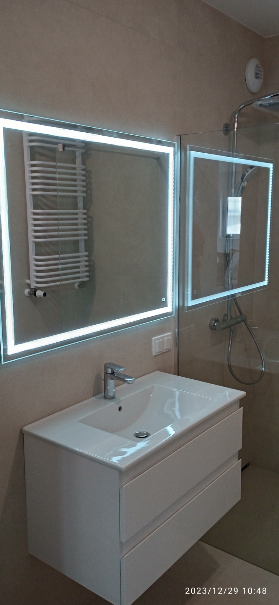 Nowoczesna łazienka z białą umywalką nablatową z szafką, podświetlanym lustrem i szklaną kabiną prysznicową z podświetleniem LED.