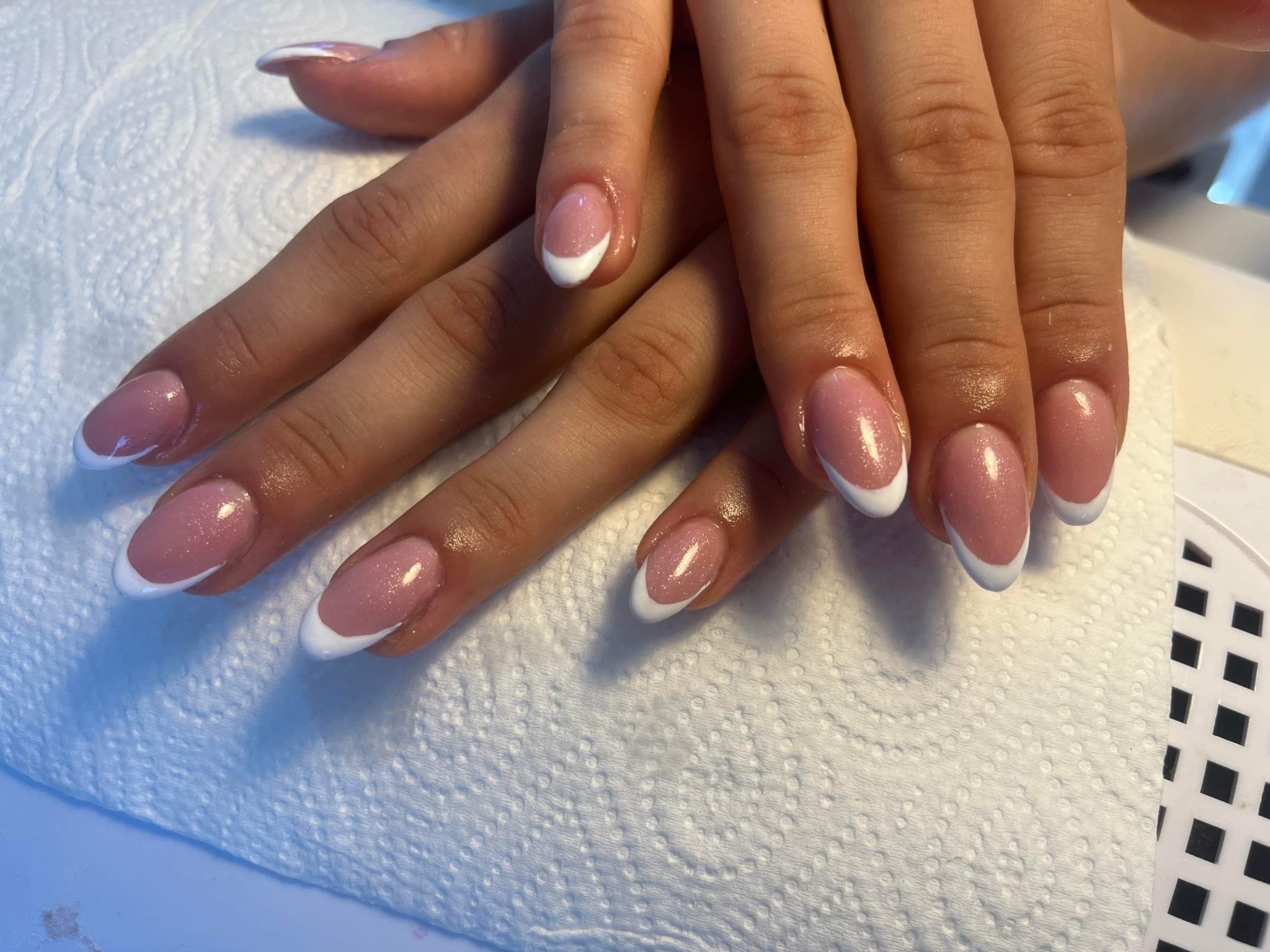 Dłonie z delikatnym, różowym lakierem i białym francuskim zdobieniem, ułożone na białym ręczniku papierowym.