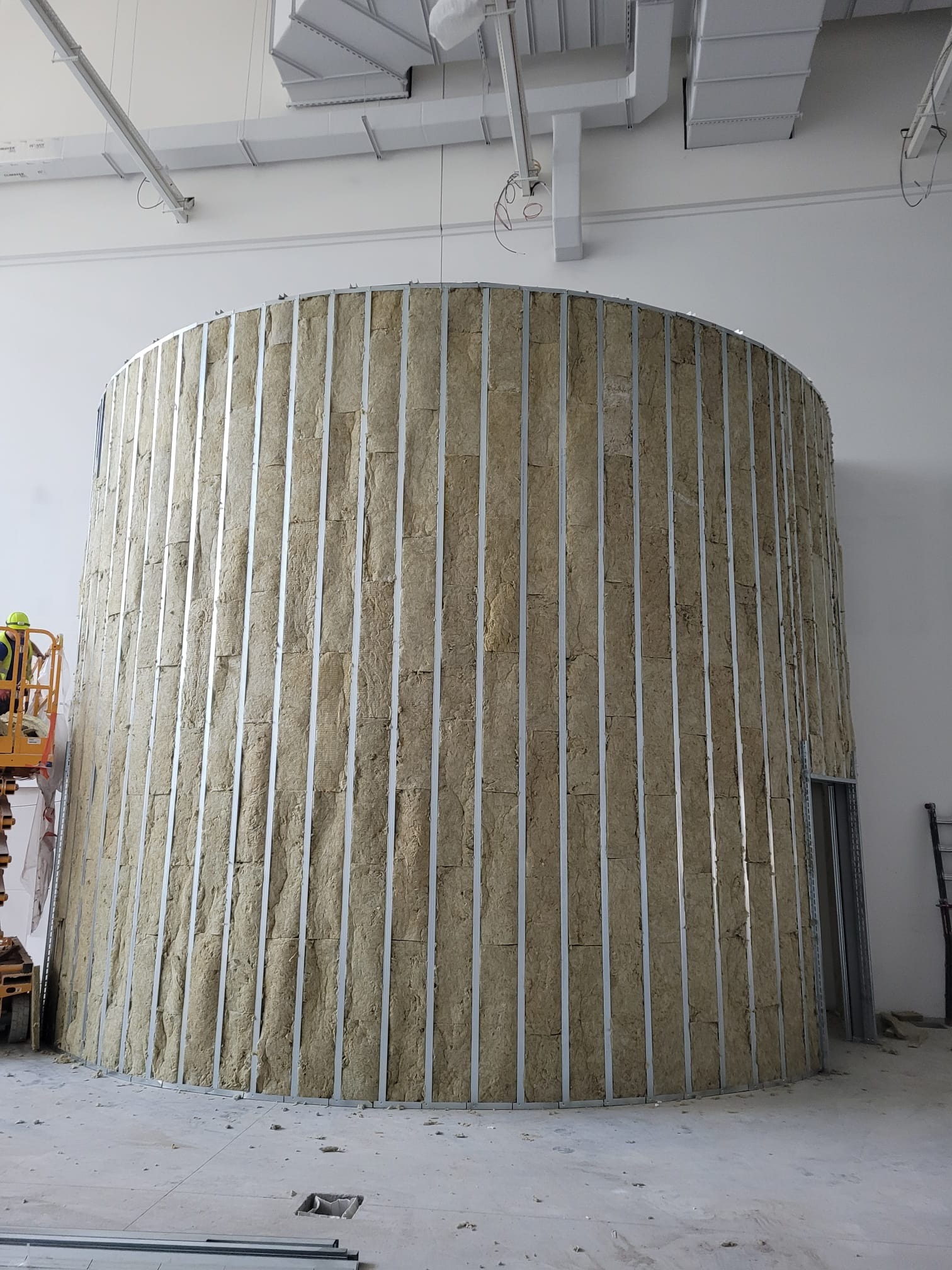 Wnętrze w Krzyszkowicach w trakcie prac wykończeniowych, widoczna konstrukcja ścianki działowej o nietypowym, zaokrąglonym kształcie z wypełnieniem izolacyjnym z wełny mineralnej w metalowym stelażu.