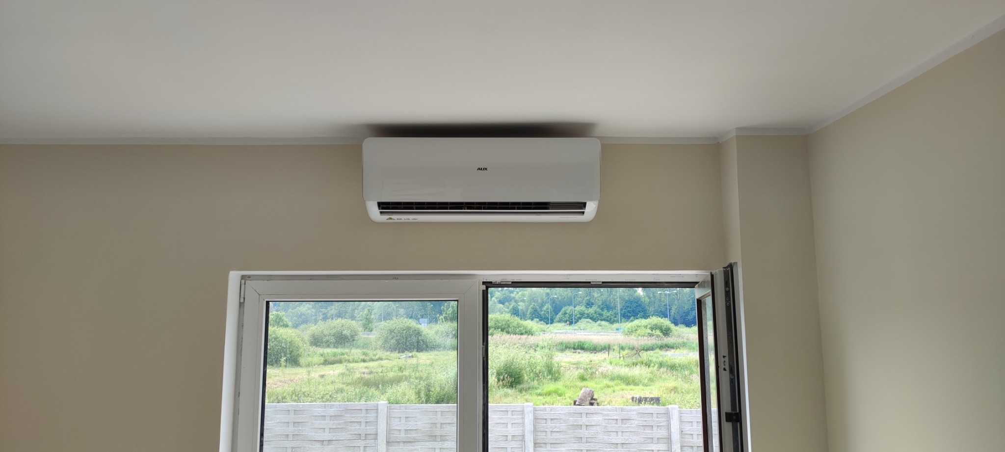 Zamontowany, biały klimatyzator AUX w domu w Lubsku, widok na zielony krajobraz za oknem.