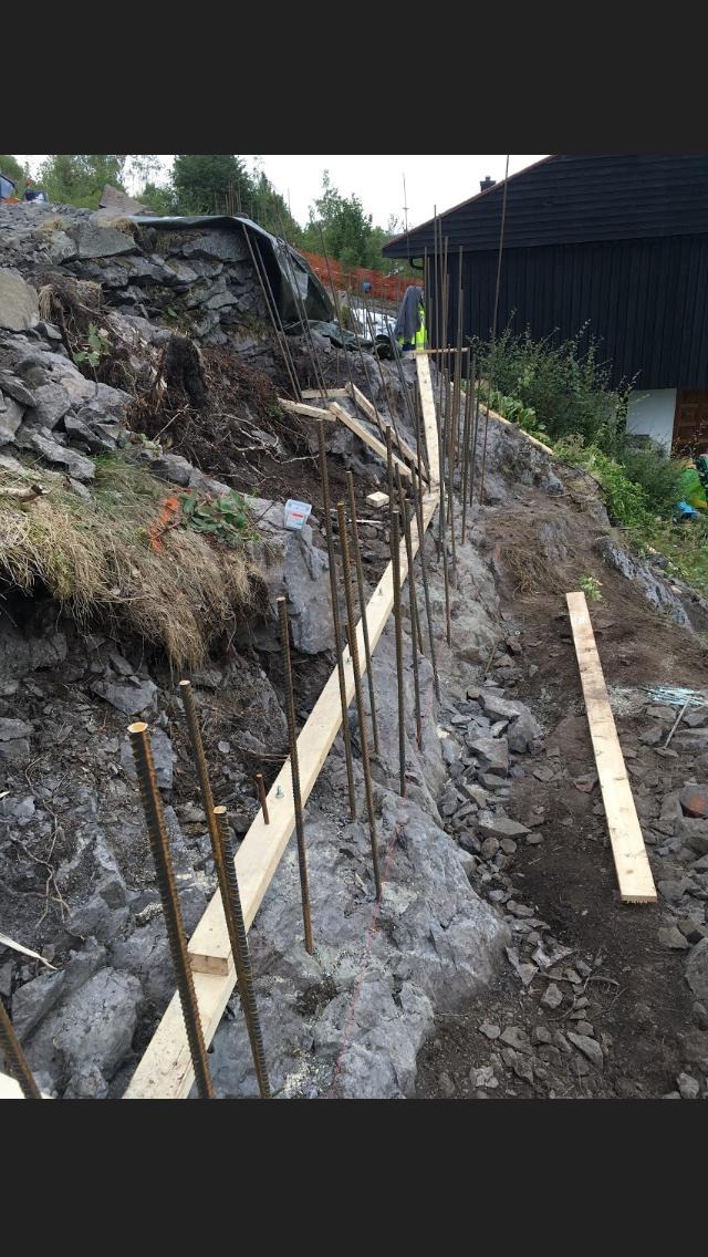 Przygotowanie zbrojenia i szalunku na skalistym zboczu pod budowę budynku żelbetowego, widoczne wystające pręty zbrojeniowe i drewniane elementy konstrukcyjne.